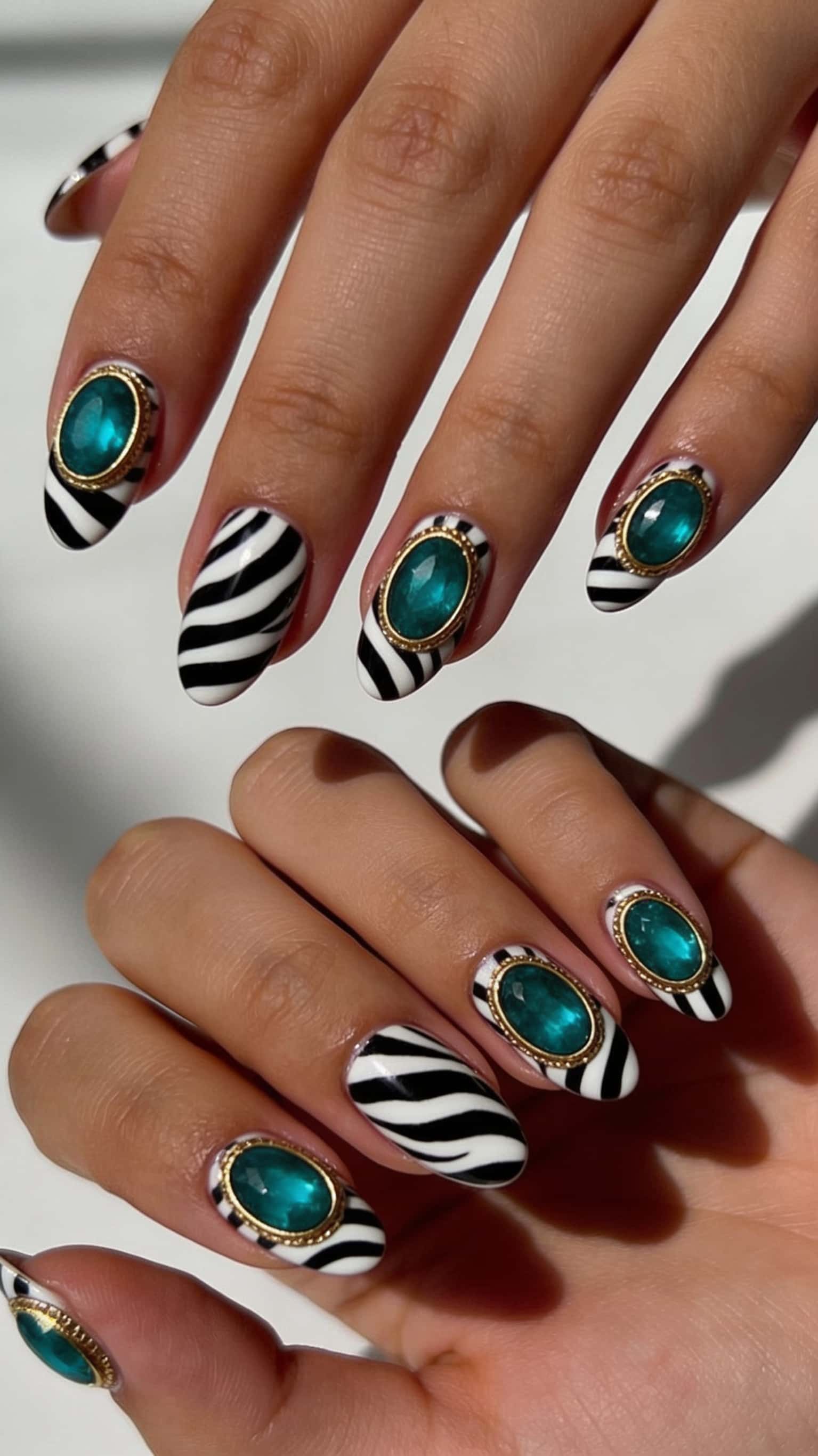 Oval nails with black and white zebra print, adorned with large emerald green jewels in gold settings.